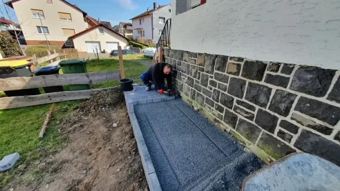 Randsteine werden vor einer Natursteinmauer gesetzt