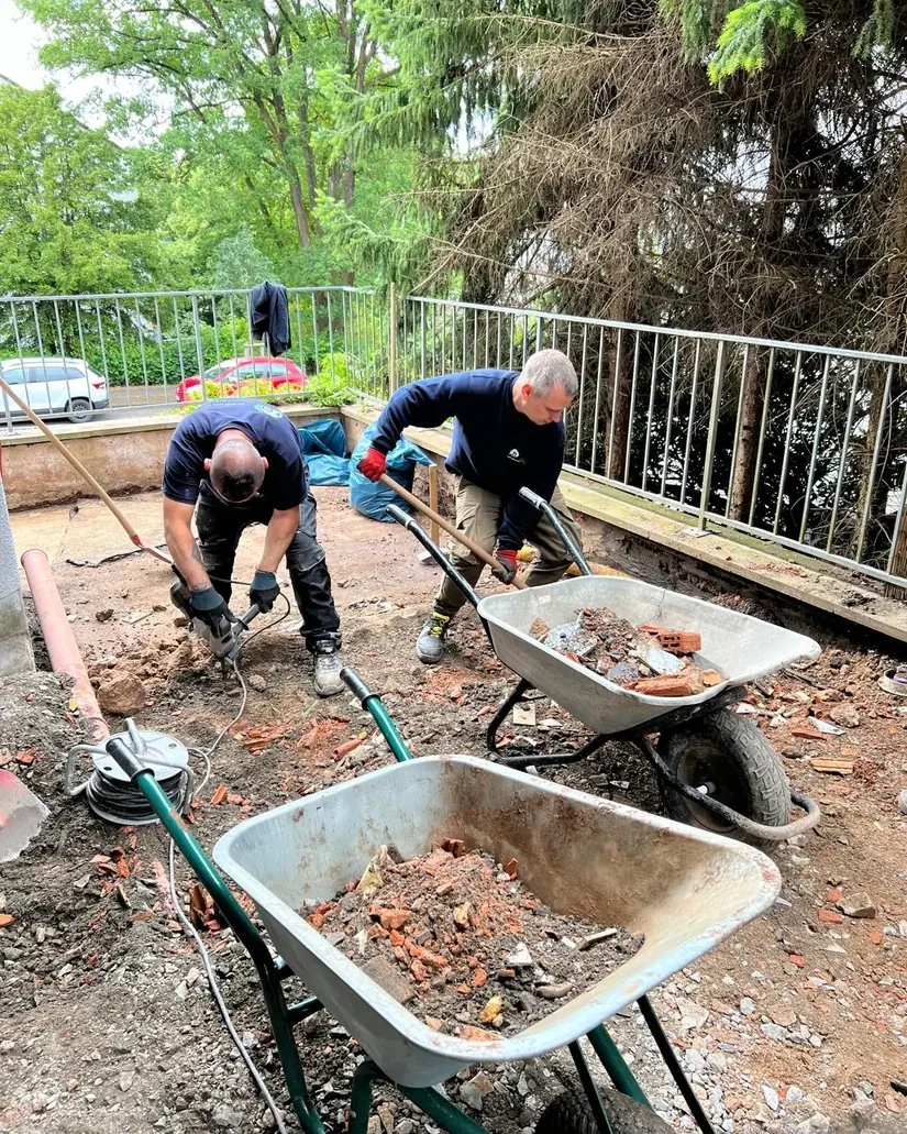 Zwei Mitarbeiter räumen den alten Aufbau in Schubkarren ab